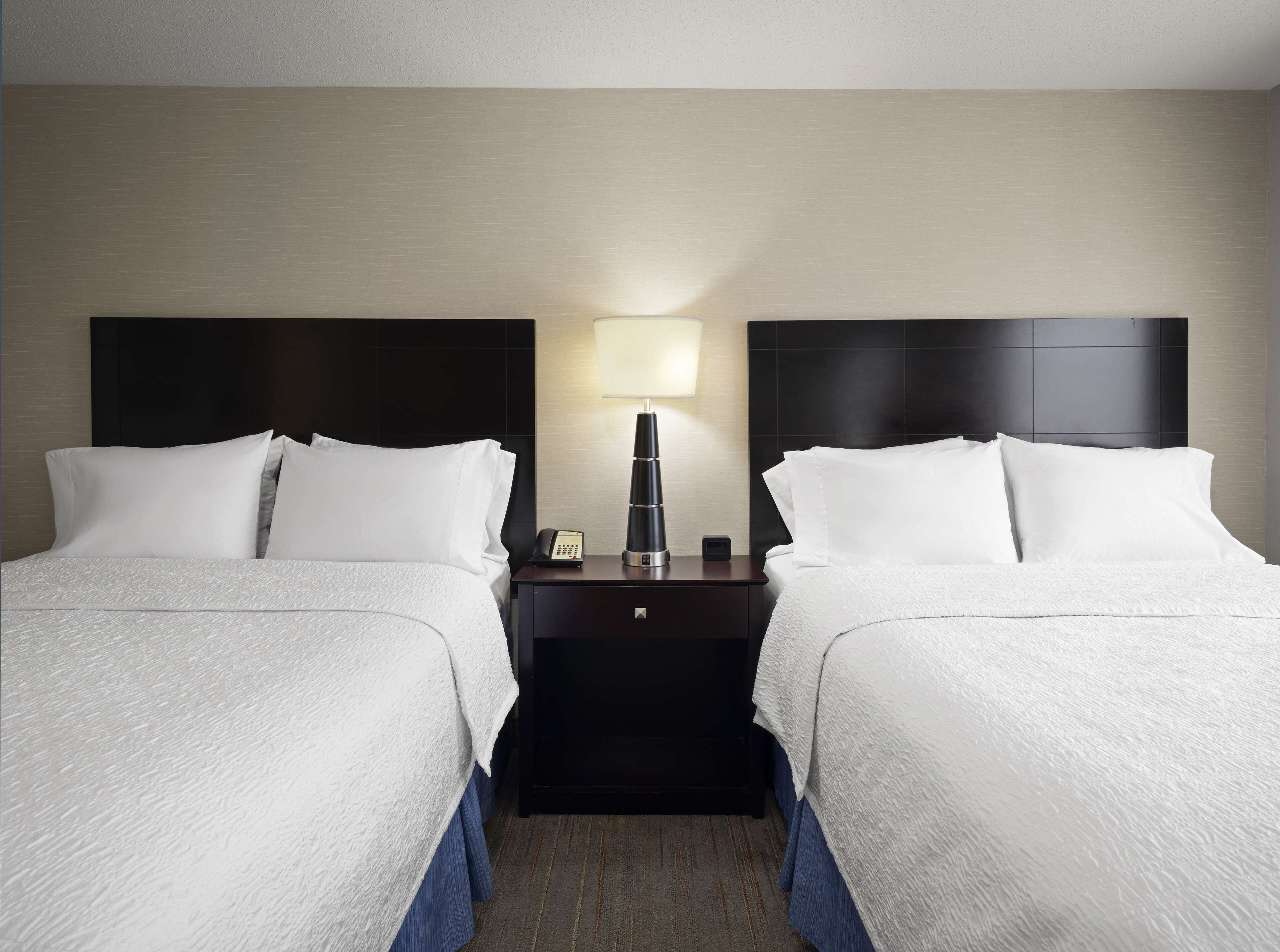 Habitación de hotel con dos camas, una mesita de noche con lámpara y tel éfono.
