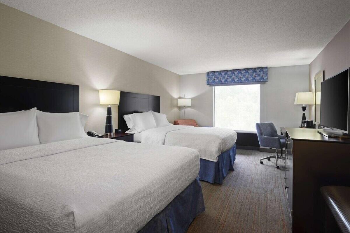 A hotel room with two beds, a desk, a chair, and a television.