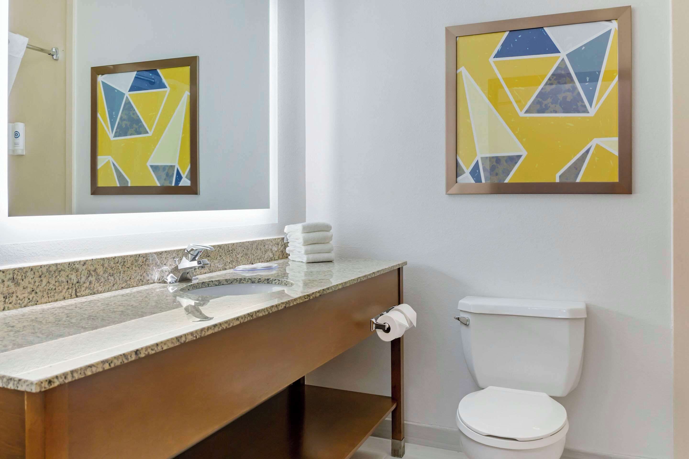 A bathroom with a granite countertop sink, a toilet, and two framed abstract paintings on the wall.