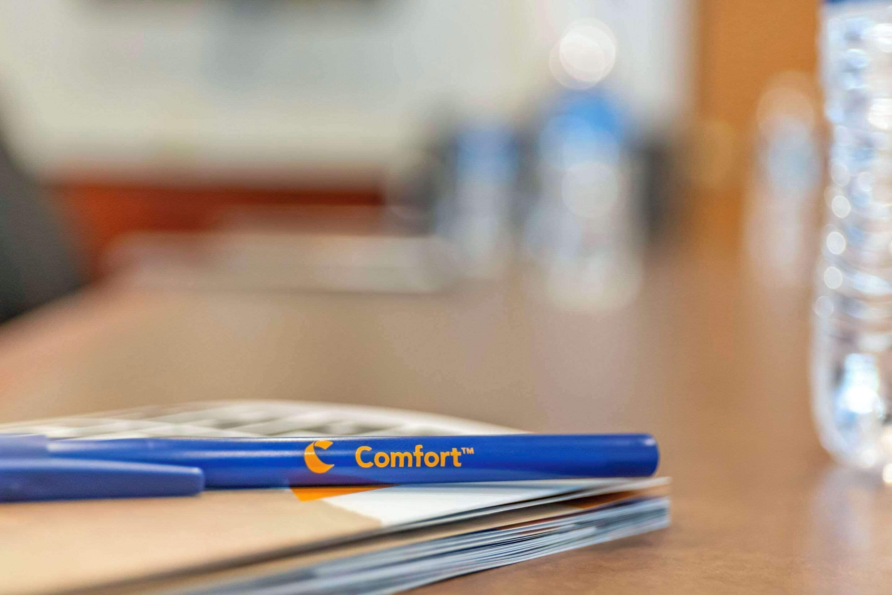 A blue pen with the word "Comfort" on a stack of papers on a wooden table.