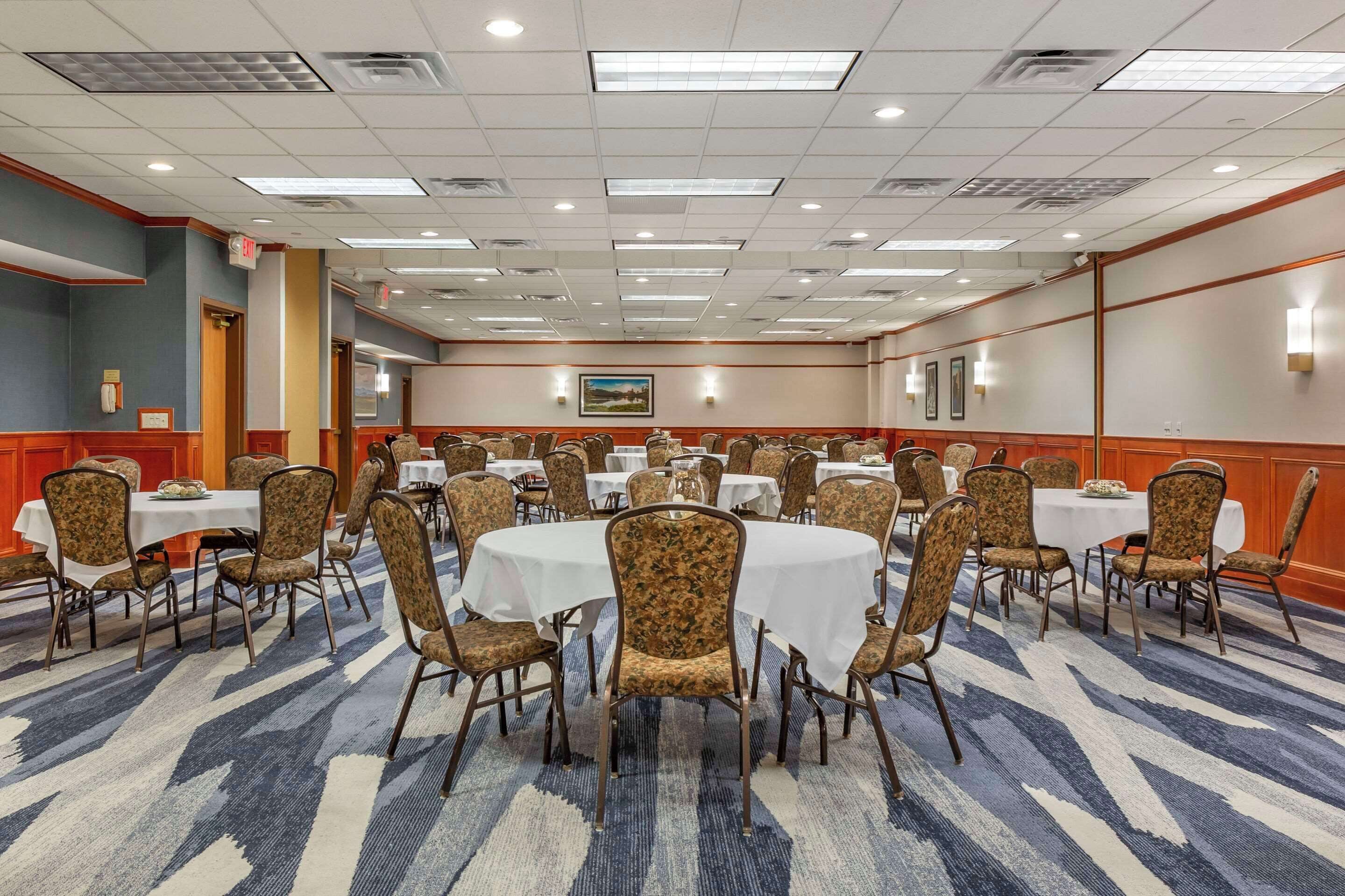 A large conference room with round tables and chairs, equipped with ceiling lights and a carpeted floor.