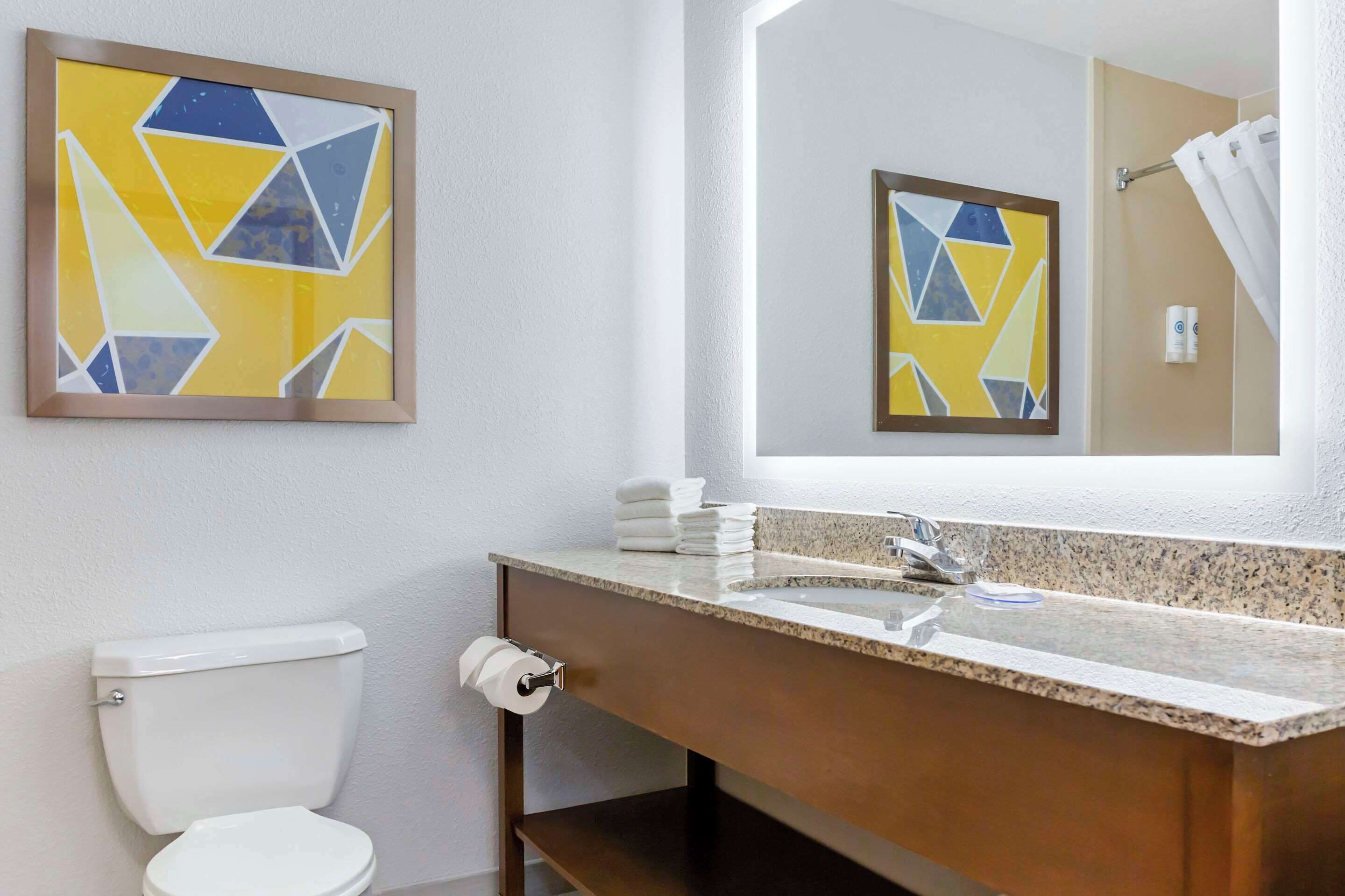 A bathroom with a white toilet, a sink with a granite countertop, and a mirror reflecting the room.