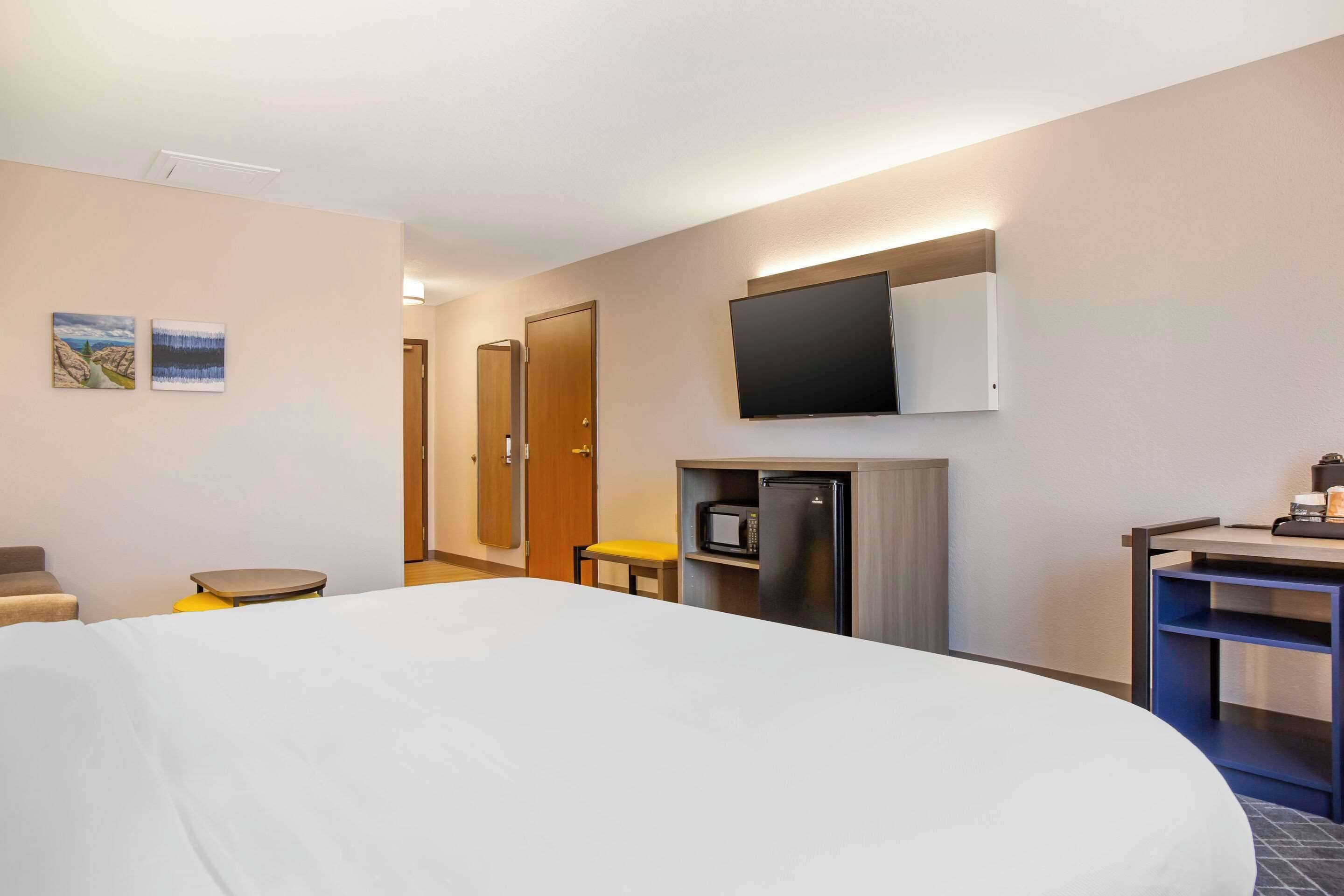 Habitación de hotel con una cama grande, un escritorio con computadora, un microondas y un televisor montado en la pared.