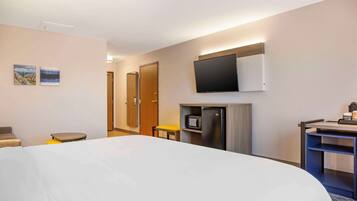 Habitación de hotel con una cama grande, un escritorio con computadora, un microondas y un televisor montado en la pared.