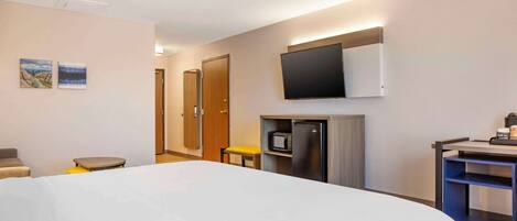 Habitación de hotel con una cama grande, un escritorio con computadora, un microondas y un televisor montado en la pared.
