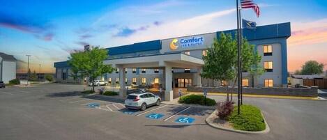 Un hotel Comfort Inn & Suites con estacionamiento, plazas de aparcamiento adaptadas para personas con discapacidad y una bandera estadounidense.