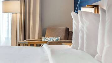 Une chambre d’hôtel avec un lit, une chaise, une lampe et une fenêtre avec des rideaux.