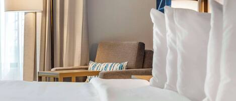 Une chambre d’hôtel avec un lit, une chaise, une lampe et une fenêtre avec des rideaux.