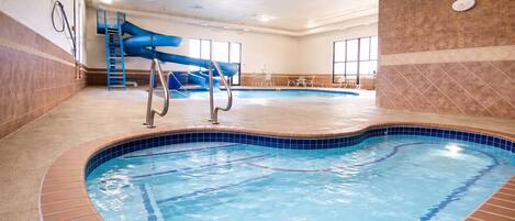 An indoor swimming pool with a blue slide, a small pool table, and a window in the background.