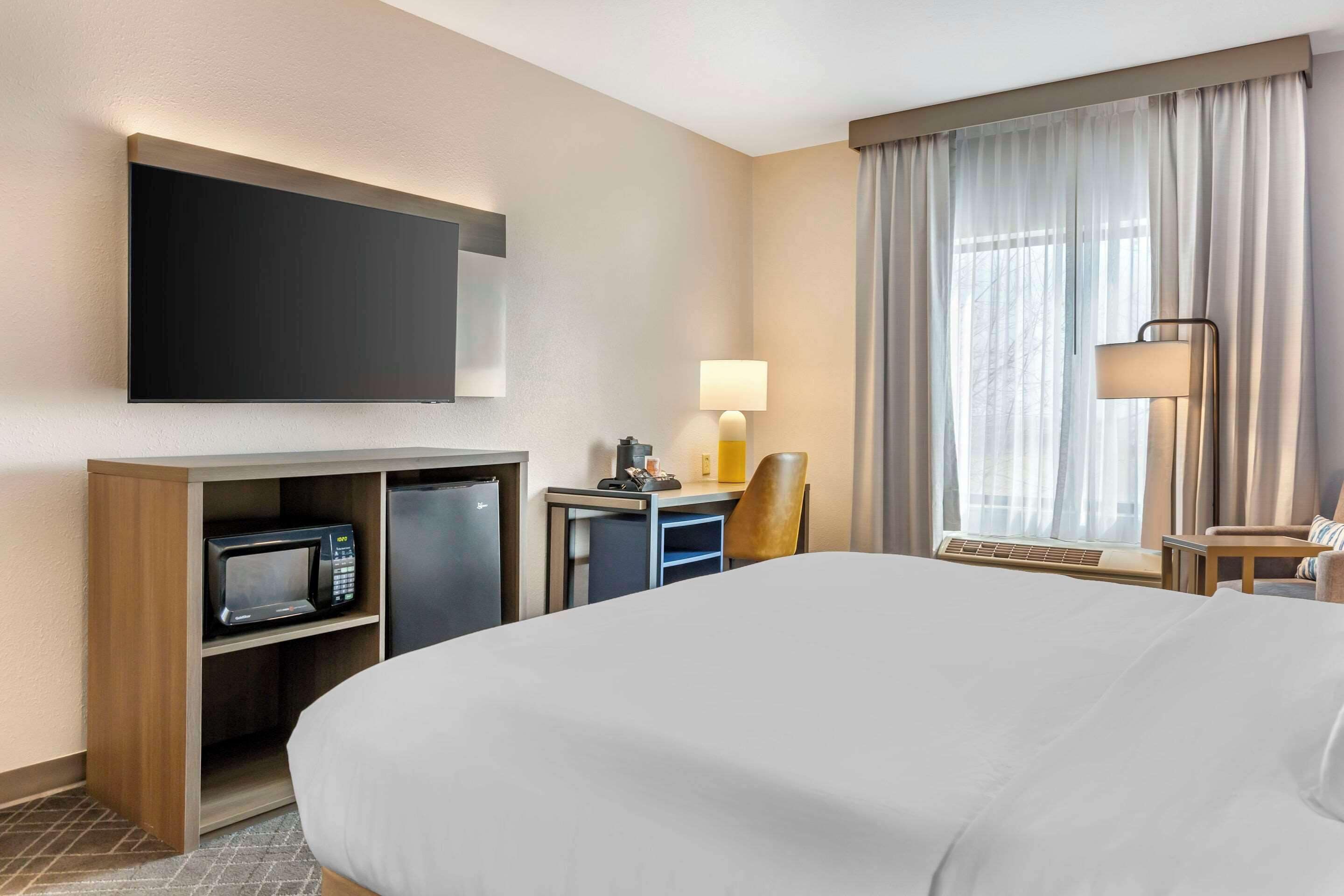 Une chambre d’hôtel avec un grand lit, un téléviseur à écran plat fixé au mur, un bureau avec une lampe, un four à micro-ondes et une chaise.