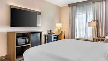 A hotel room with a large bed, a flat-screen TV mounted on the wall, a desk with a lamp, a microwave, and a chair.