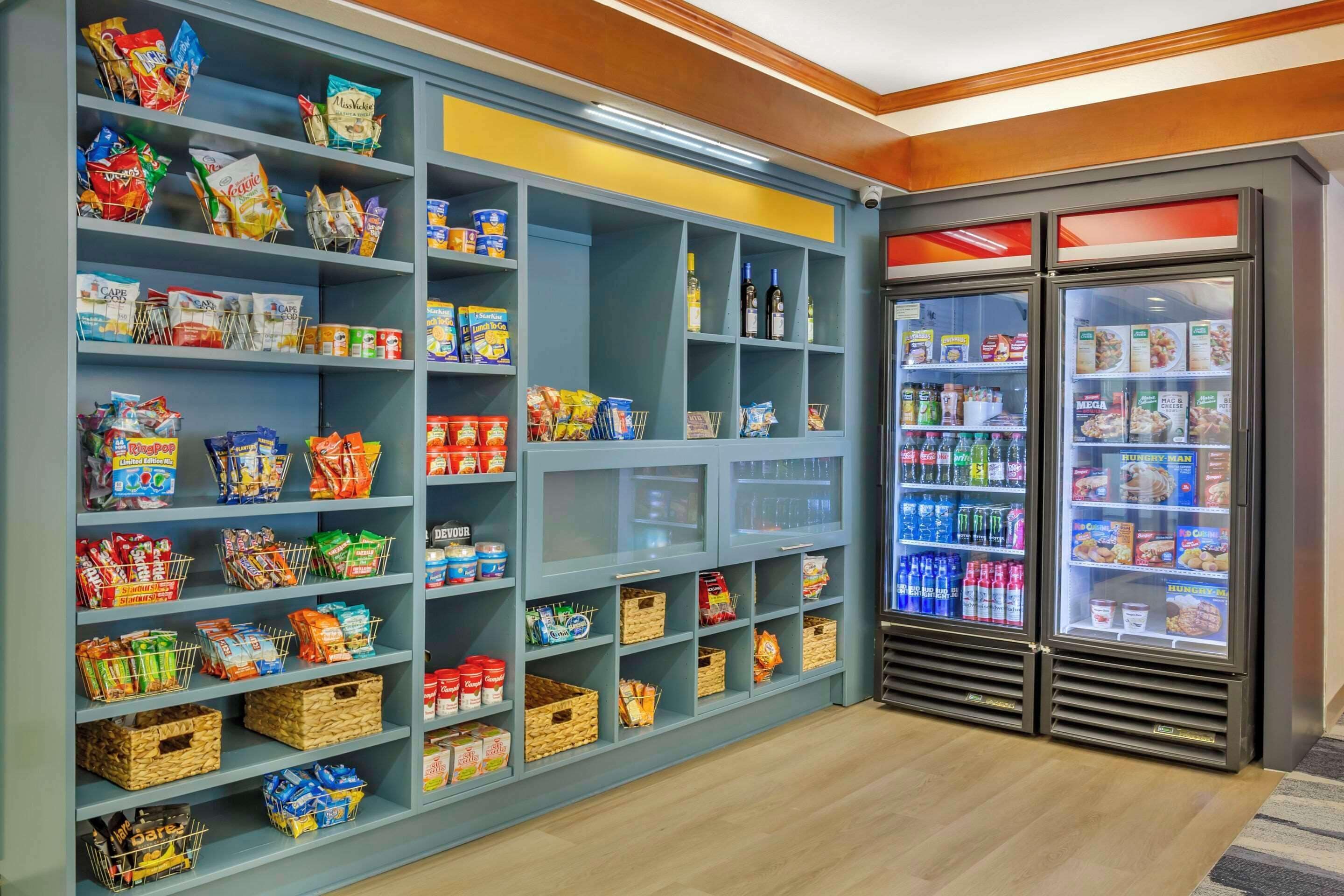 Zona de aperitivos y bebidas con estantes llenos de snacks, refrescos y helados.