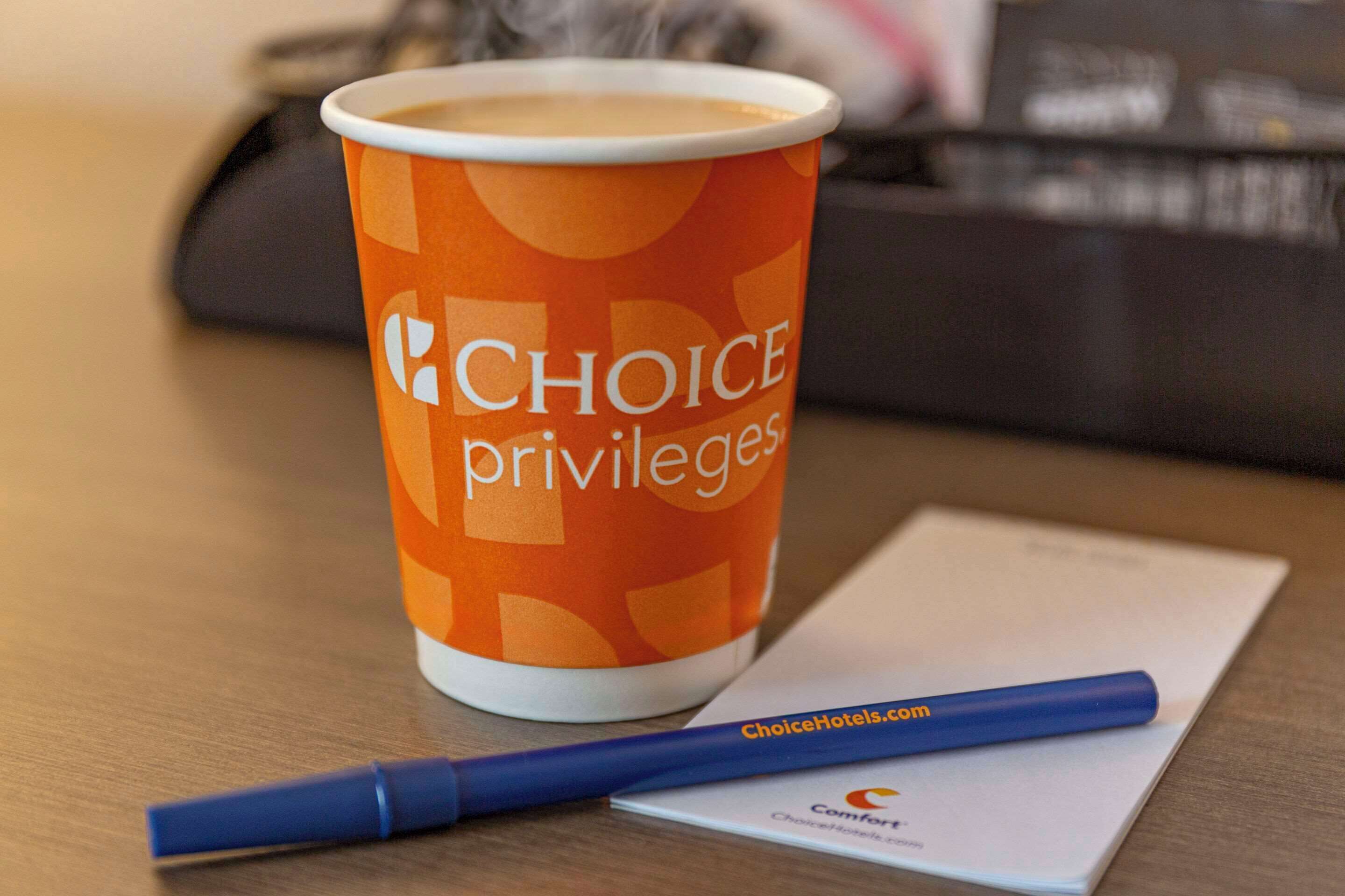 A paper cup with "Choice Privileges" branding, a blue pen, and a business card on a wooden table.