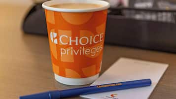 Paperinen kahvikuppi, jossa on «Choice Privileges» -brändin logo, sininen kynä ja käyntikortti puupöydällä.