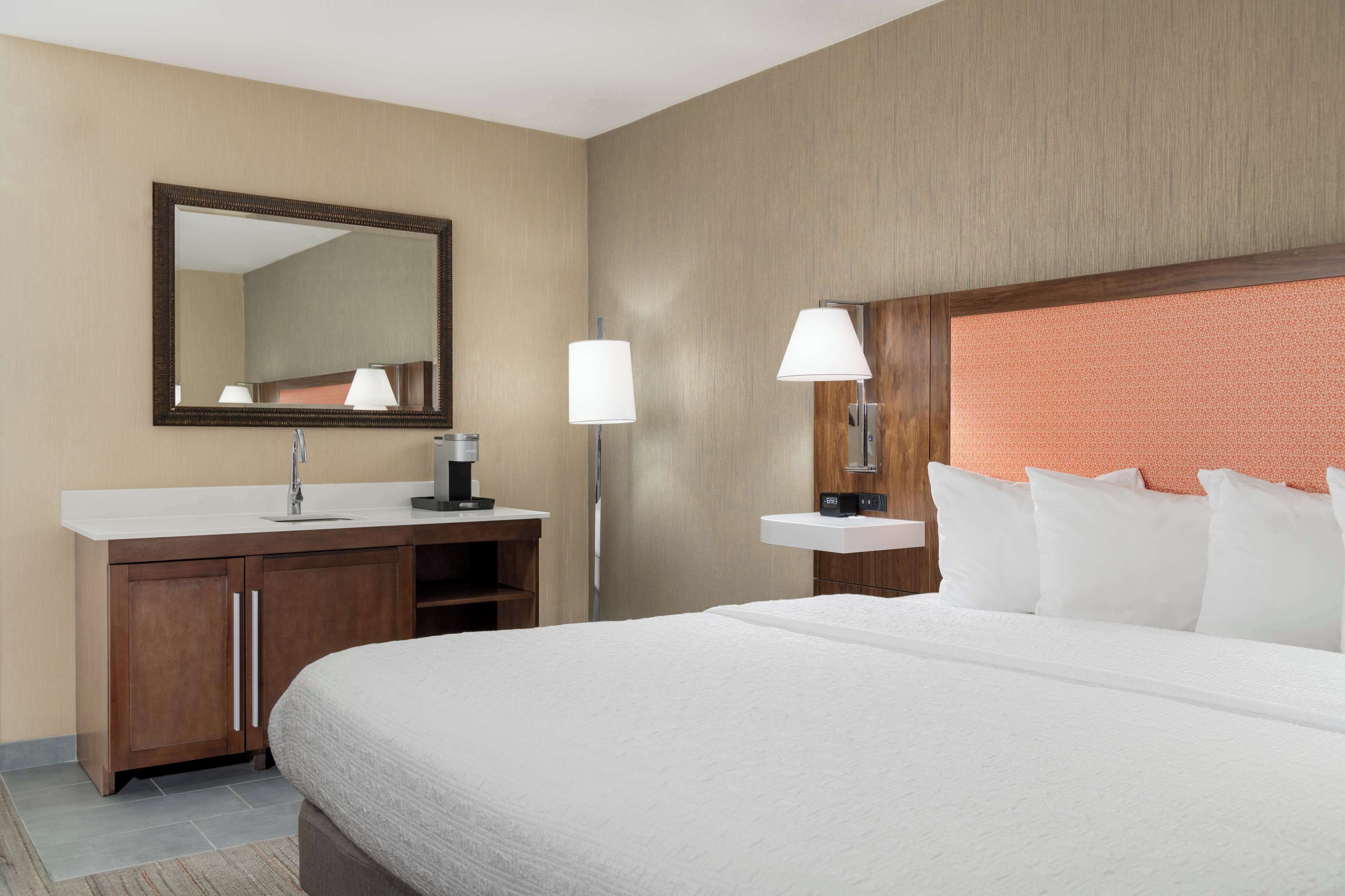 A hotel room with a large bed, a wooden cabinet with a sink, a mirror, and two wall-mounted lamps.
