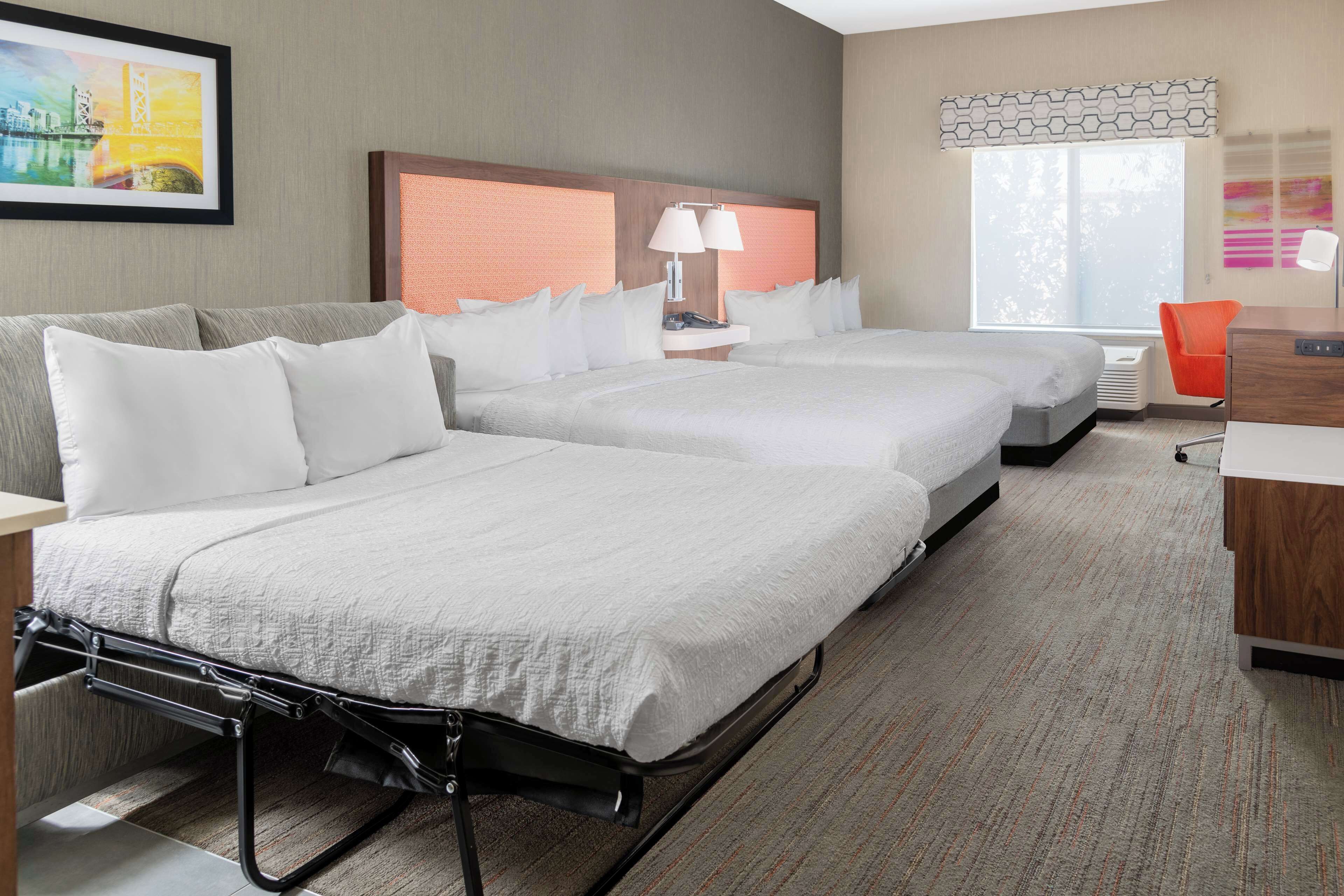 A hotel room with two beds, a desk, a chair, and a window with a view.