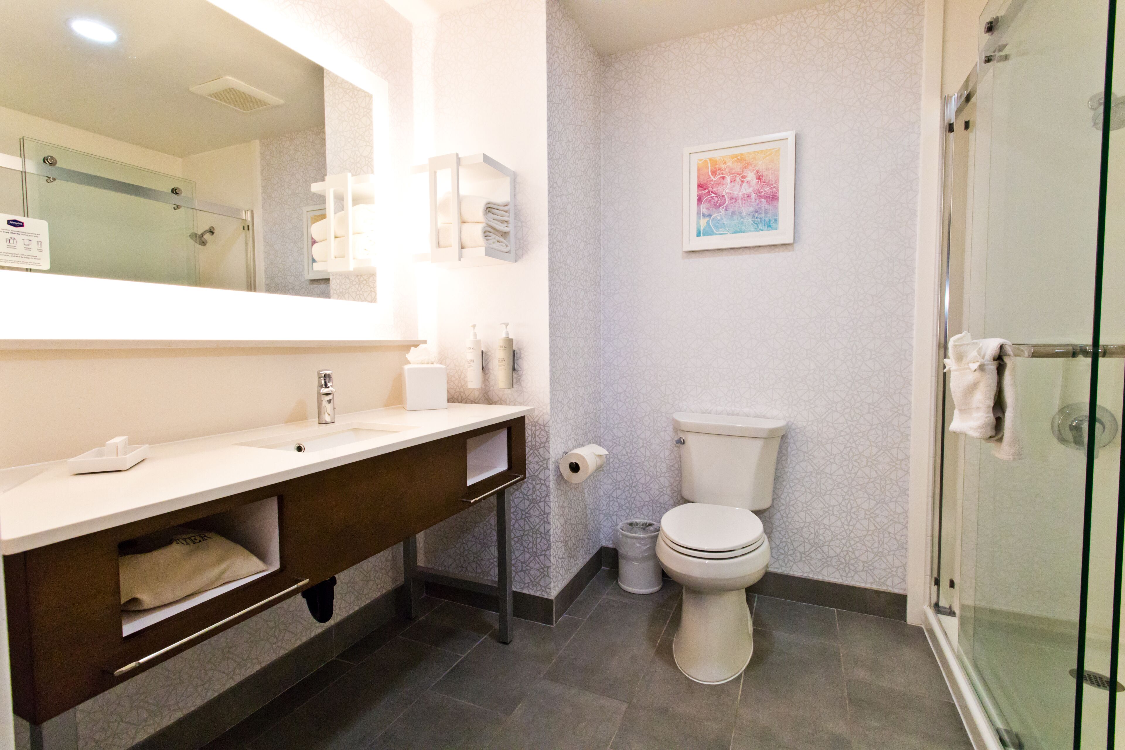 Un baño moderno con cabina de ducha de vidrio, inodoro blanco y tocador con espejo.