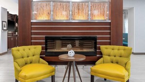 A modern living room with a fireplace, two yellow armchairs, and a round table with a decorative object. - Hampton Inn & Suites Sacramento-Cal Expo (Sacramento)