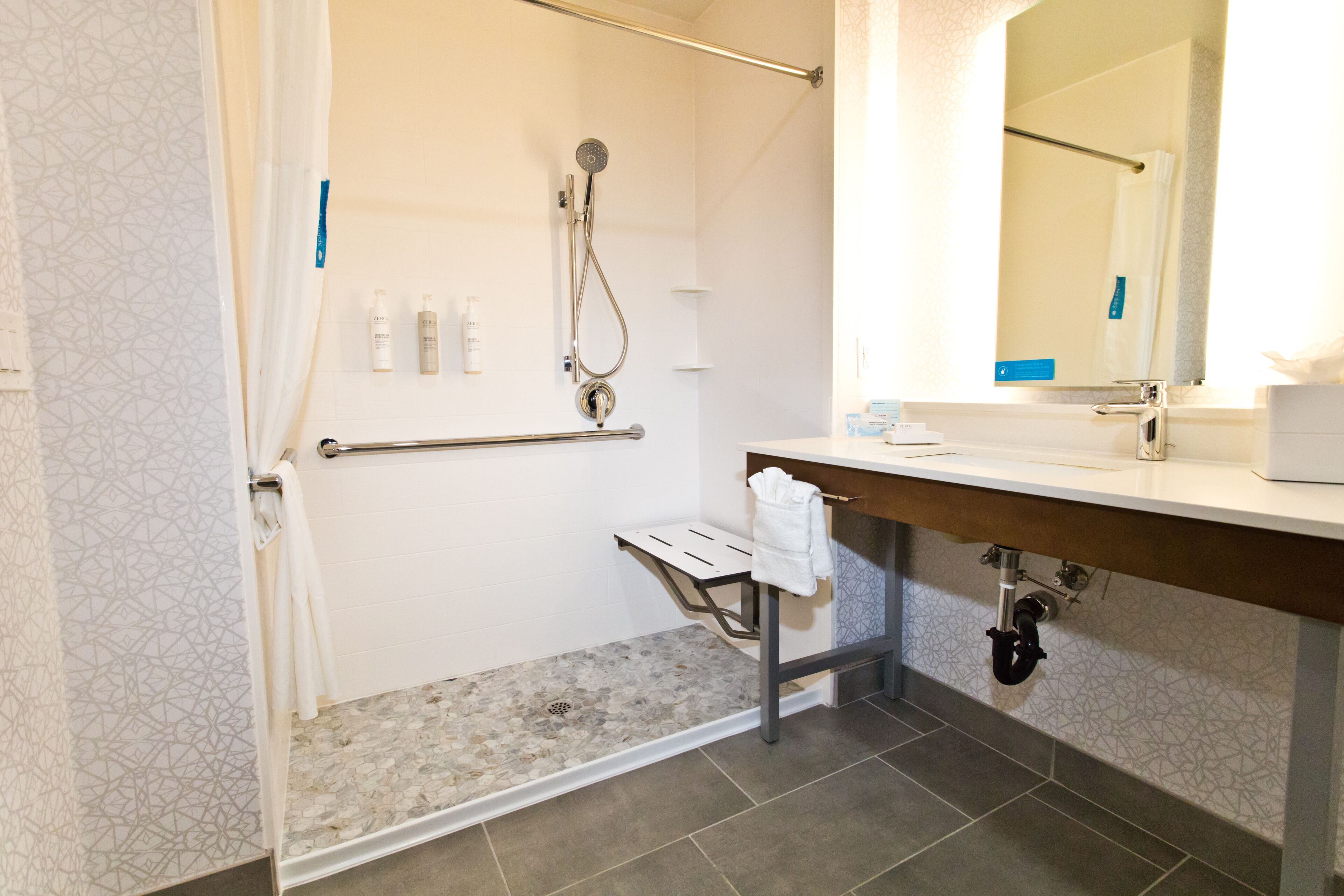 Une salle de bain moderne équipée d’une douche, d’une barre d’appui et d’un meuble-lavabo avec un miroir.
