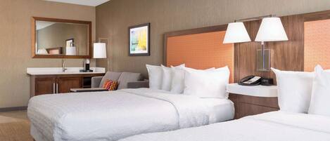 A hotel room with two beds, a bathroom with a sink, and a nightstand with a phone and lamp.