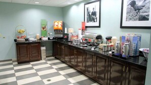 A hotel kitchen with a checkered floor, a coffee machine, and various food items on the counter. - Hampton Inn Williamston (Williamston)