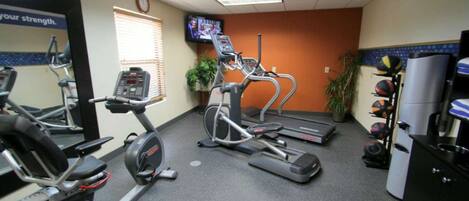 Un gimnasio con cintas de correr, elípticas y un televisor en la pared.