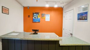A reception area with a counter, a framed certificate on the wall, and informational posters. - Motel 6 Ilion, NY (Ilion)