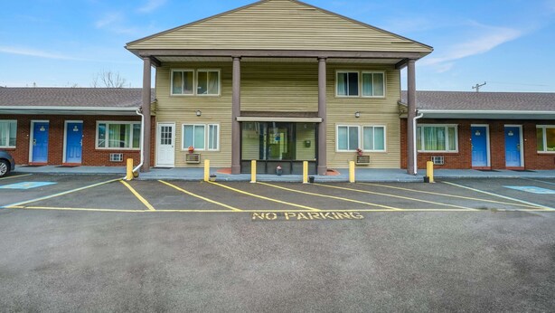 A motel with a central entrance, a parking lot marked with 'NO PARKING', and a brick facade. - Motel 6 Ilion, NY (Ilion)