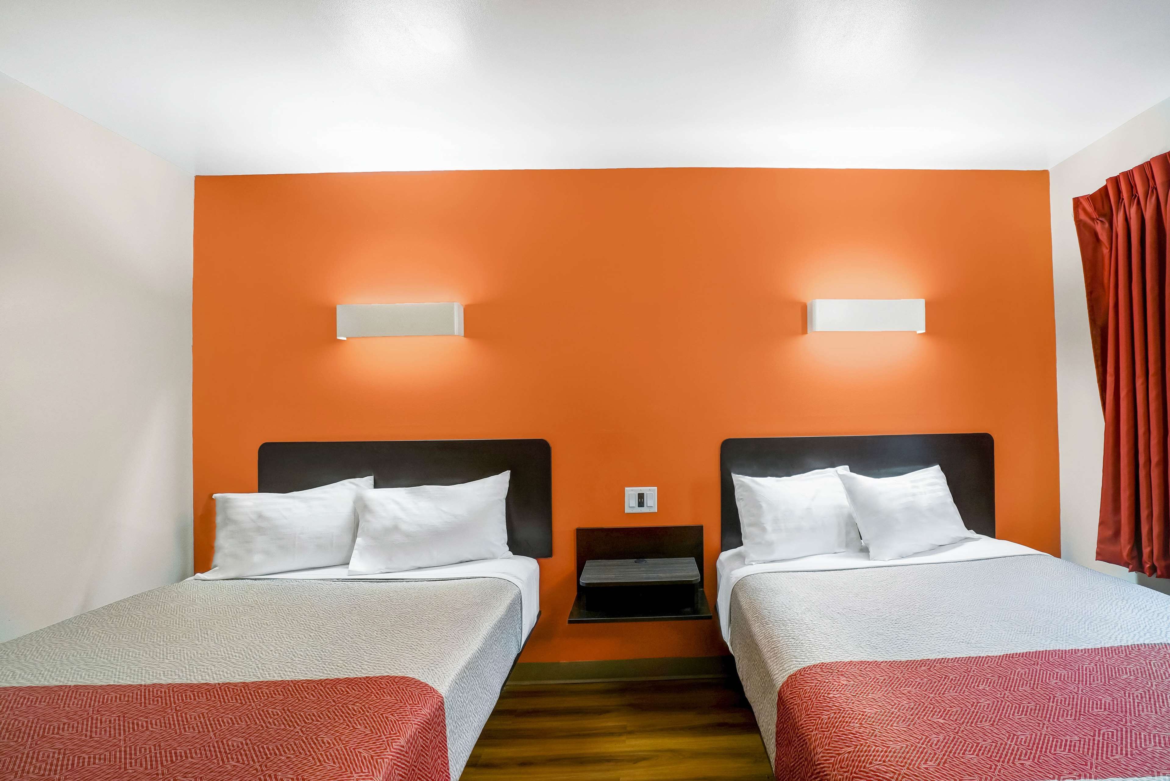 Une chambre d’hôtel avec deux lits, des murs orange, du linge de lit blanc et une petite table de chevet.