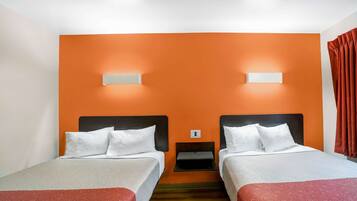 Une chambre d’hôtel avec deux lits, des murs orange, du linge de lit blanc et une petite table de chevet.