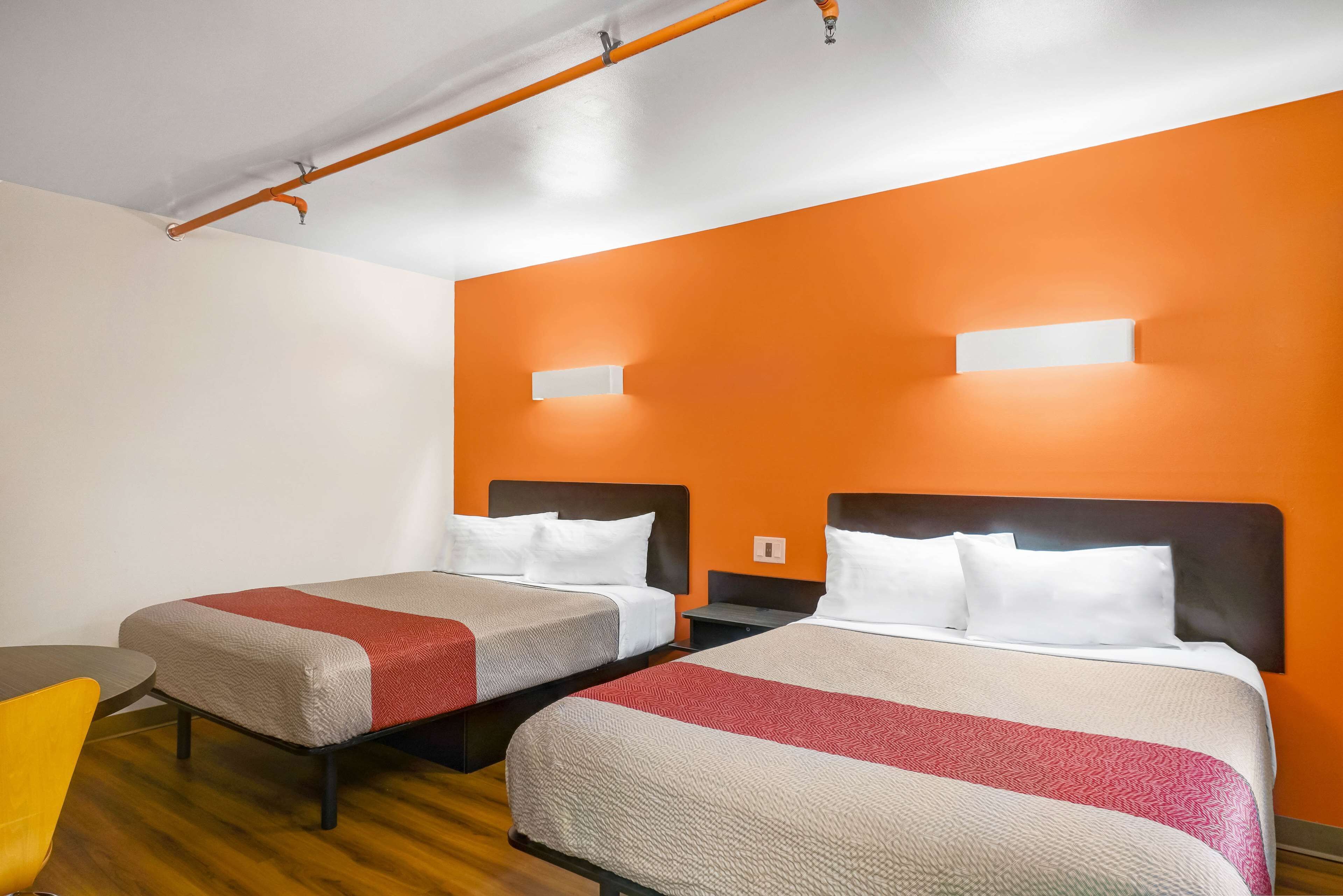 A hotel room with two beds, a wooden floor, and an orange accent wall.