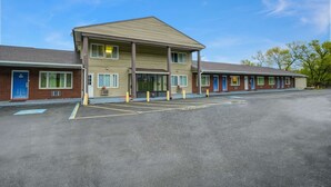 A motel with a central entrance, individual rooms on either side, and a parking lot. - Motel 6 Ilion, NY (Ilion)