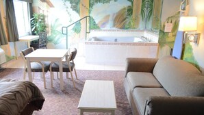 A hotel room with a sofa, a small table, a dining table with chairs, a bathtub, and a mural of a waterfall. - Scottish Inns & Suites at NRG Park (Houston)