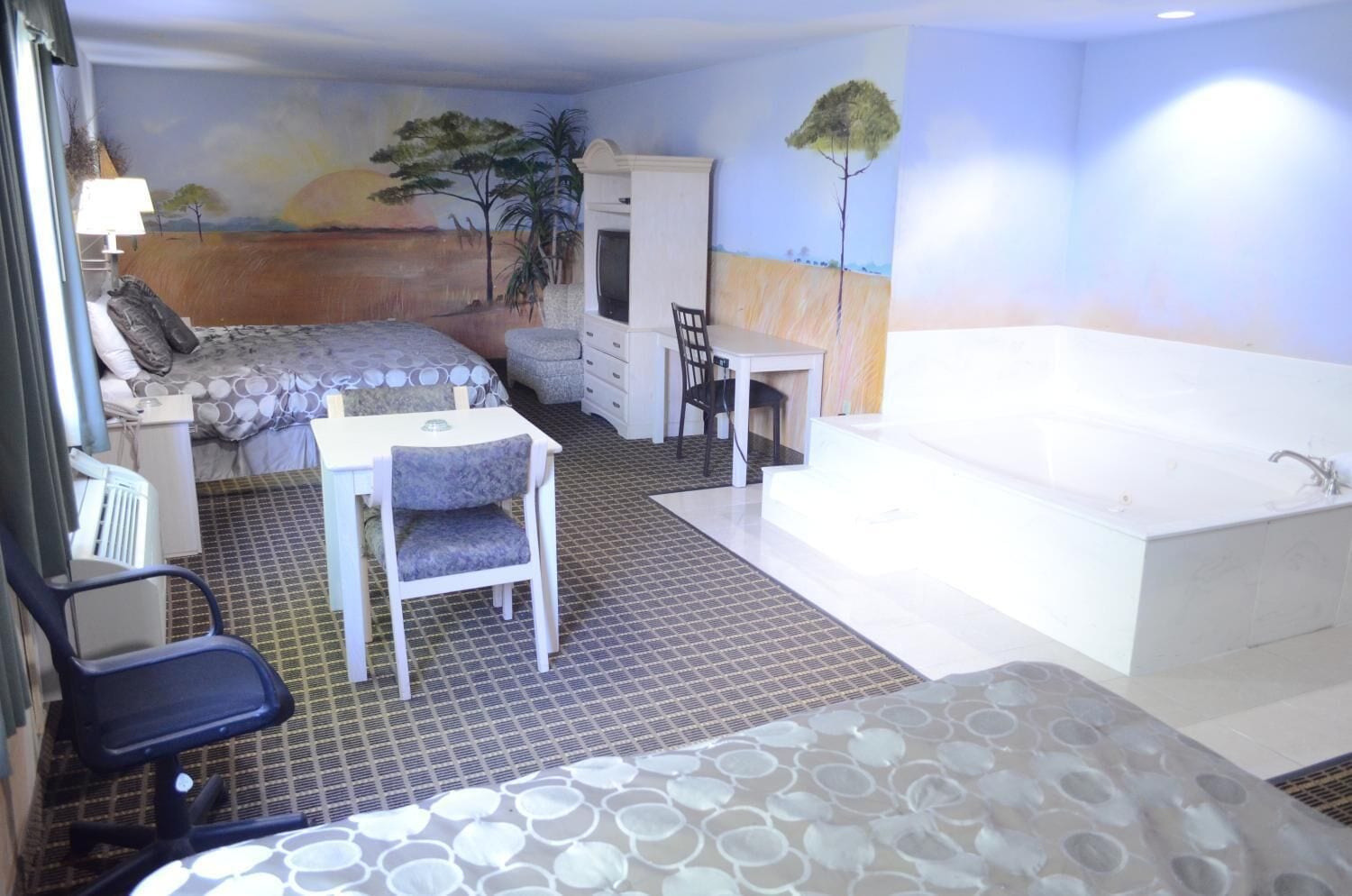 A room with a bed, a desk, a chair, a small table, and a bathtub.