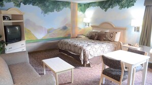 A hotel room with a bed, a sofa, a small table, and a TV. - Scottish Inns & Suites at NRG Park (Houston)
