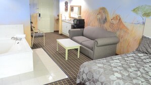 A hotel room with a large bed, a sofa, a small table, a bathroom with a bathtub, and a mural of lions. - Scottish Inns & Suites at NRG Park (Houston)