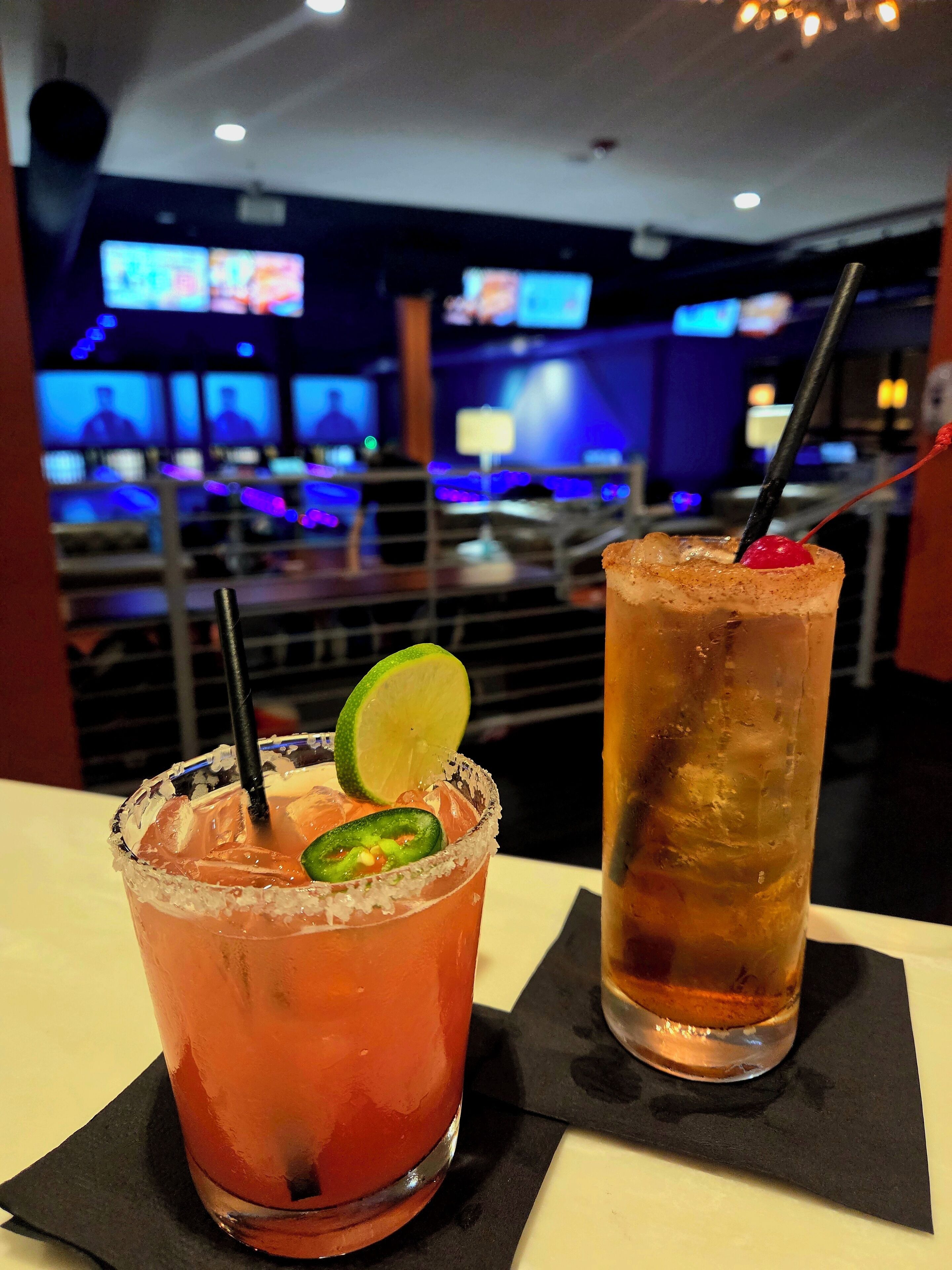 Two cocktails on a table with a bar in the background.
