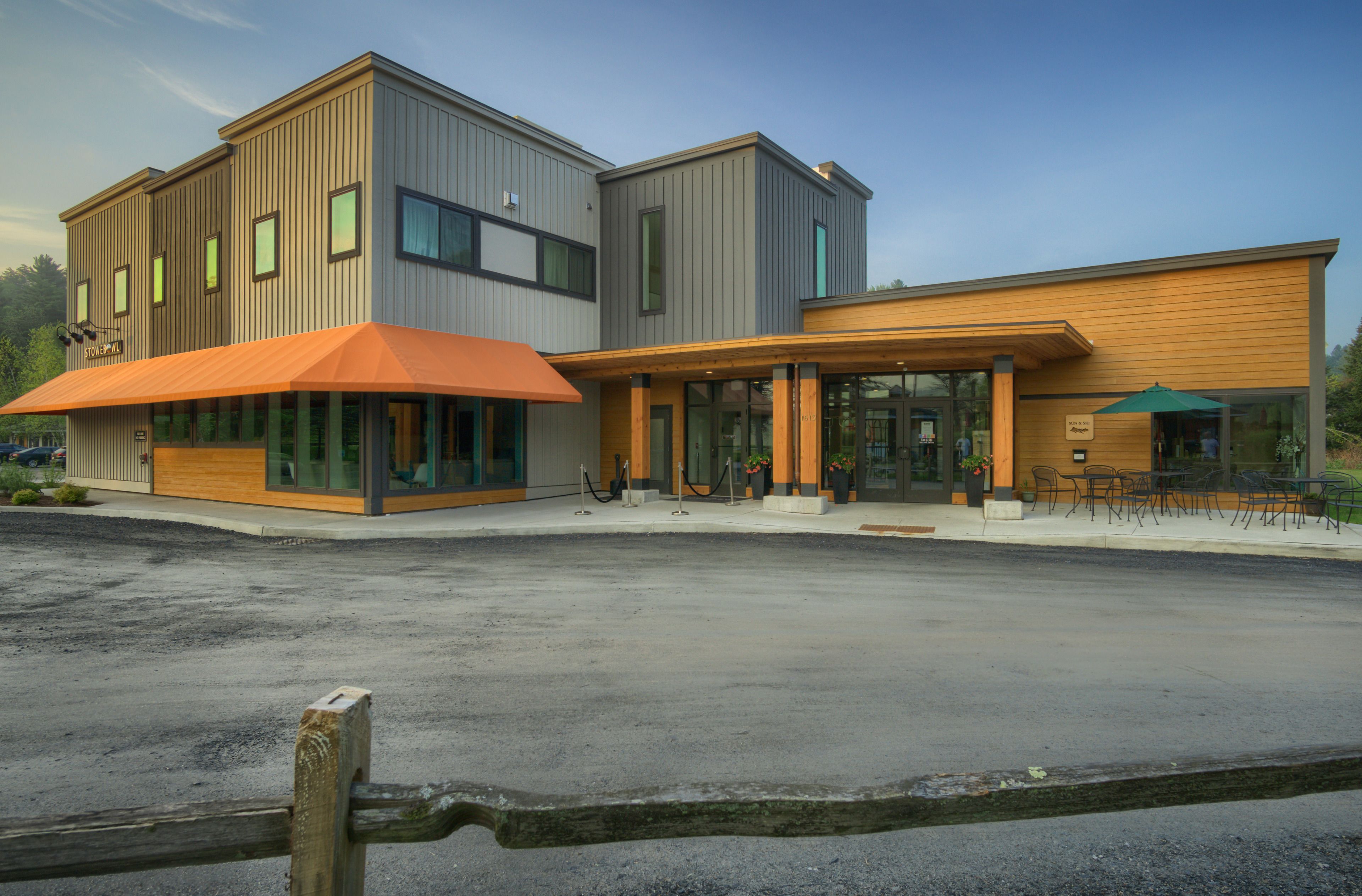 A modern building with a flat roof, large windows, and an outdoor seating area.