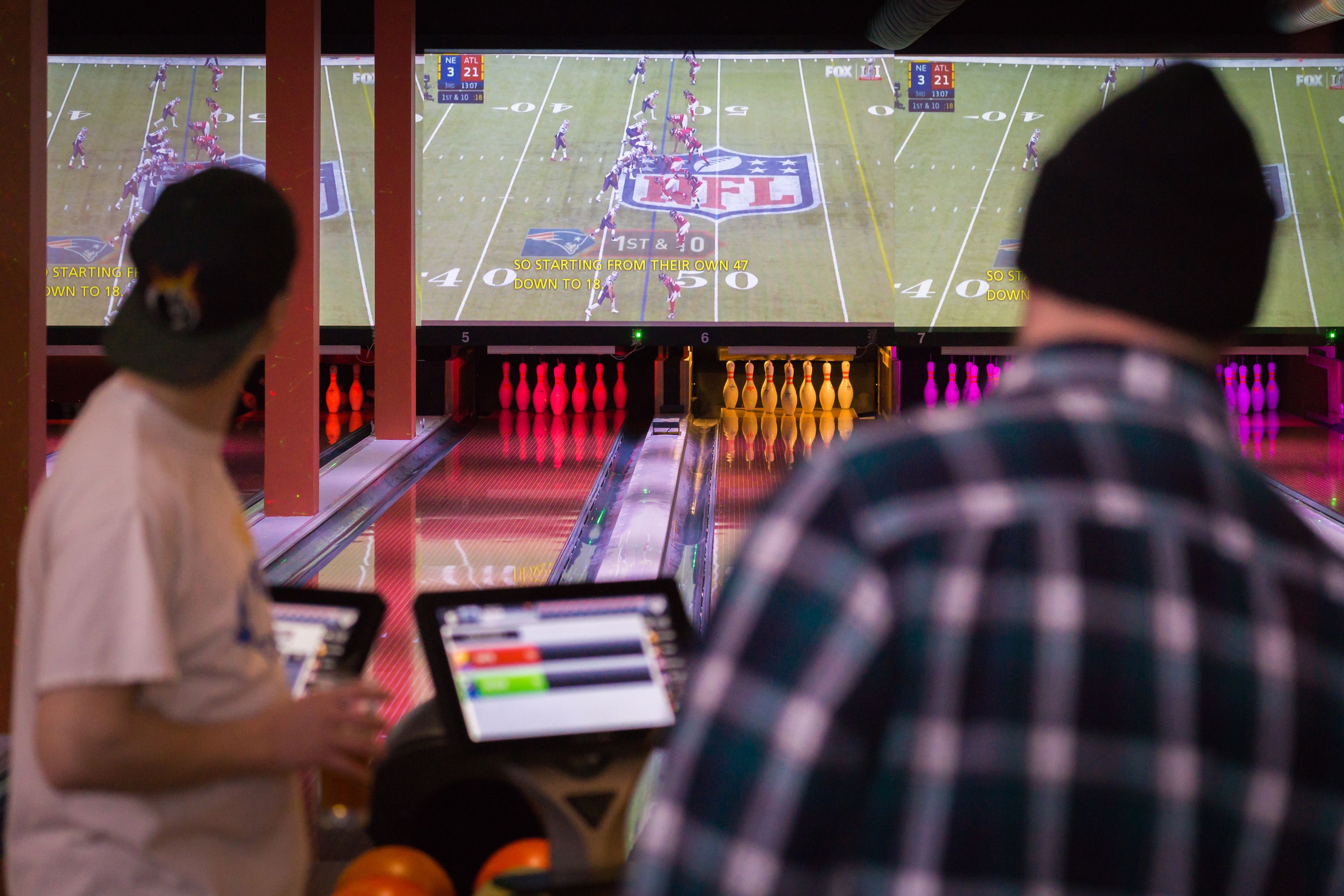 A bowling alley with multiple lanes and a large screen displaying a football game.