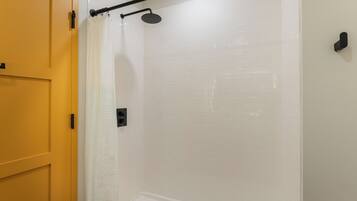Une douche avec un mur recouvert de carreaux blancs, une pomme de douche noire et un rideau de douche blanc.