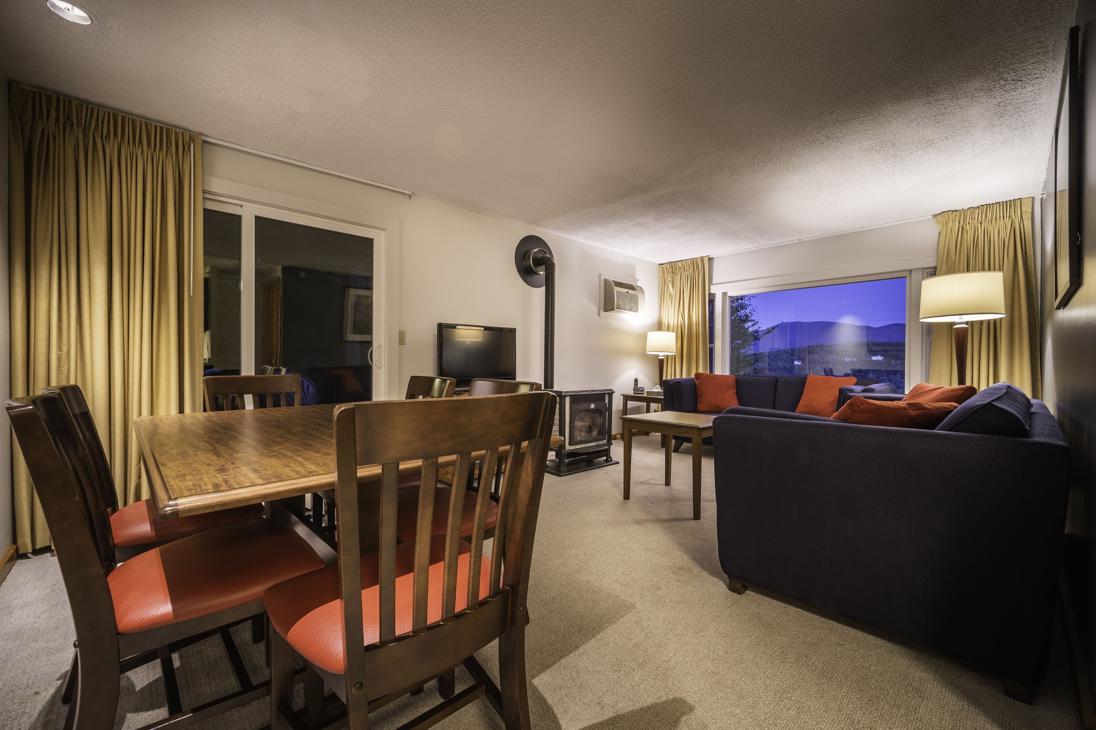 Habitación de hotel con una mesa de comedor, sillas, un sofá, un televisor y una ventana con cortinas.