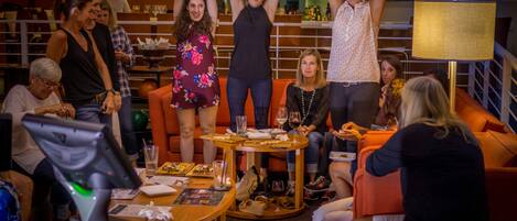 Un grupo de personas en un ambiente social, con una zona de bar, asientos y una mesa con comida y bebidas.