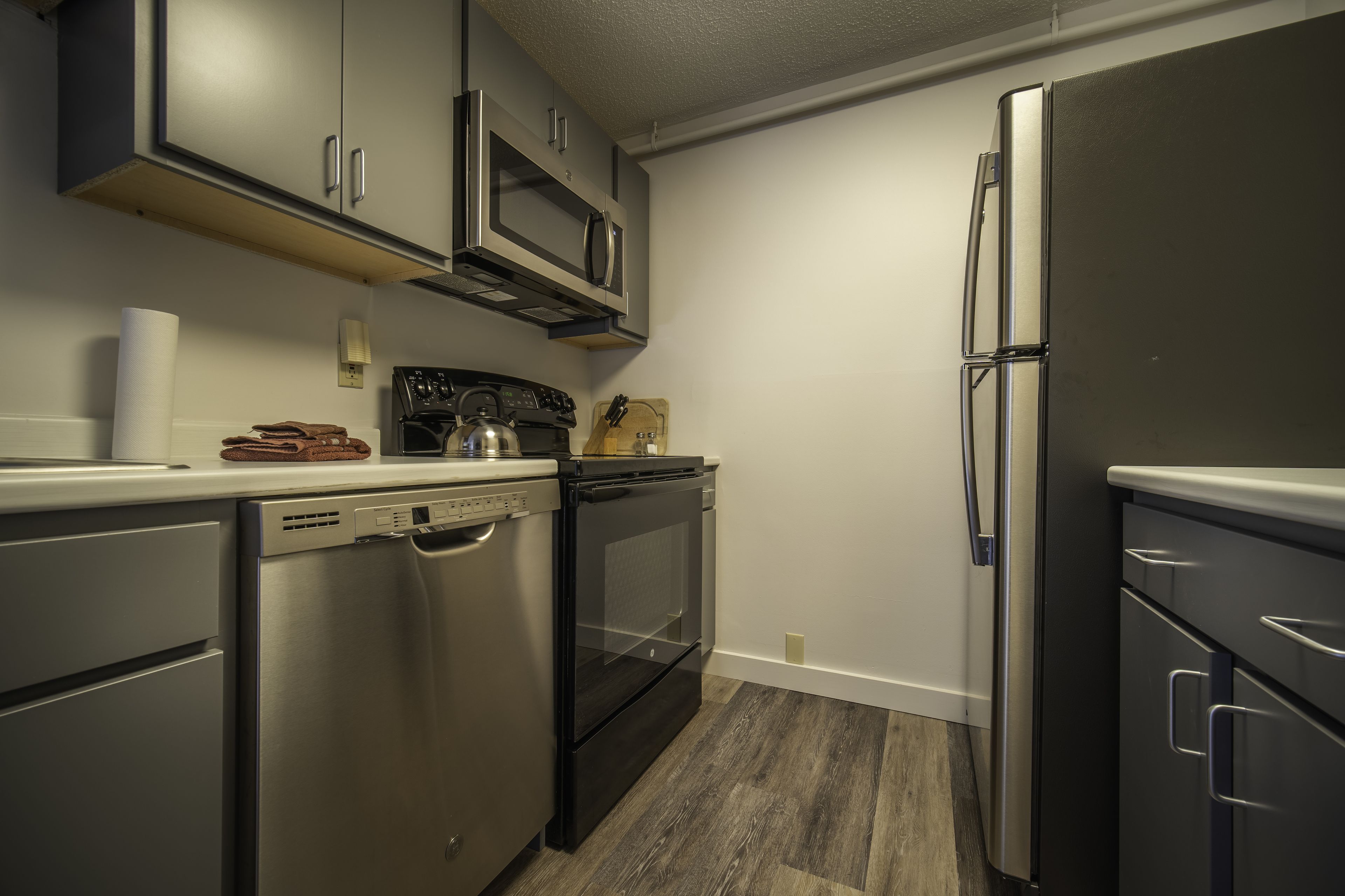 Una cocina compacta con electrodomésticos de acero inoxidable, incluyendo lavavajillas, horno, microondas y refrigerador.