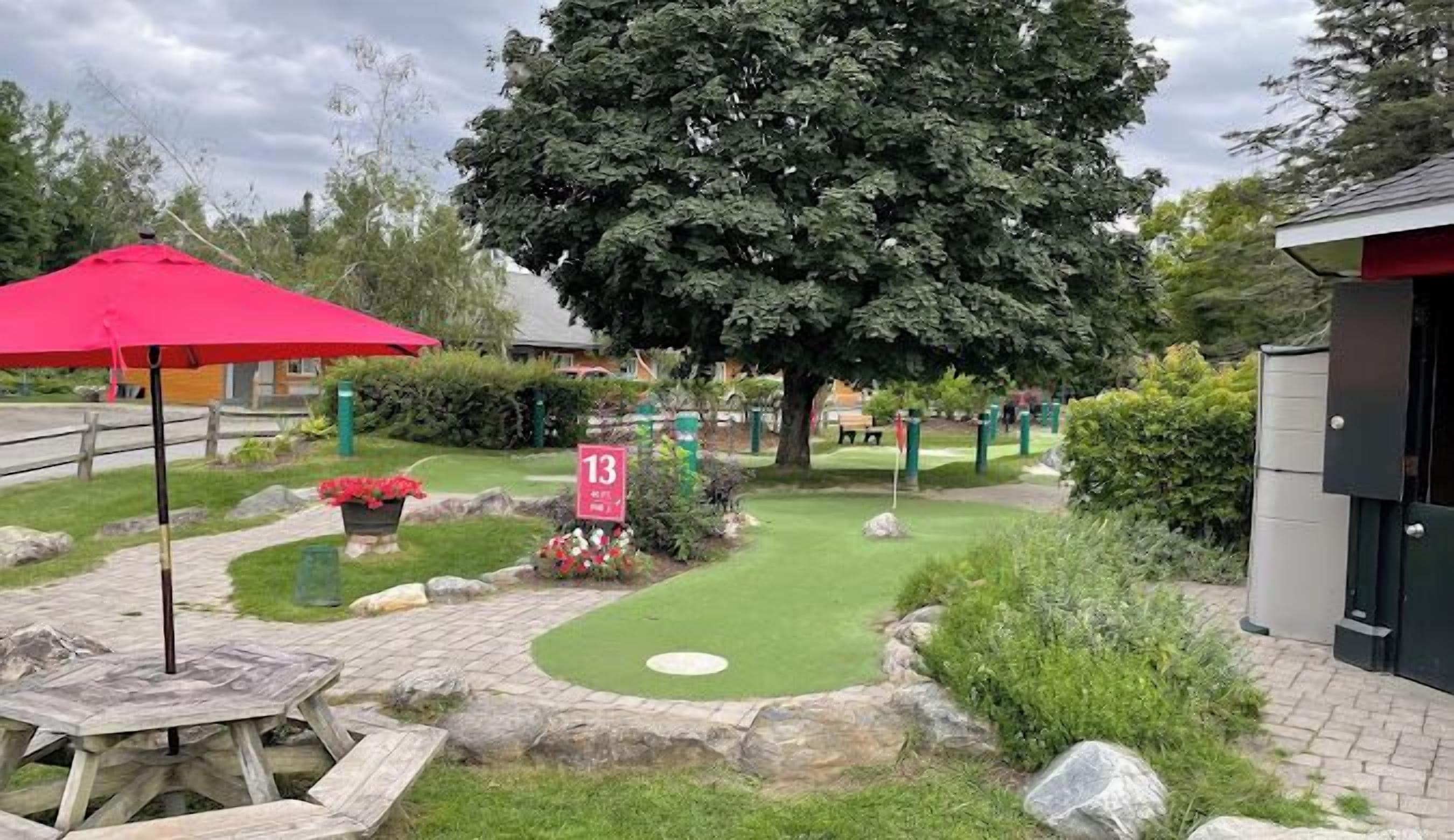 A well-maintained garden area with a red umbrella, a numbered sign, and a large tree.