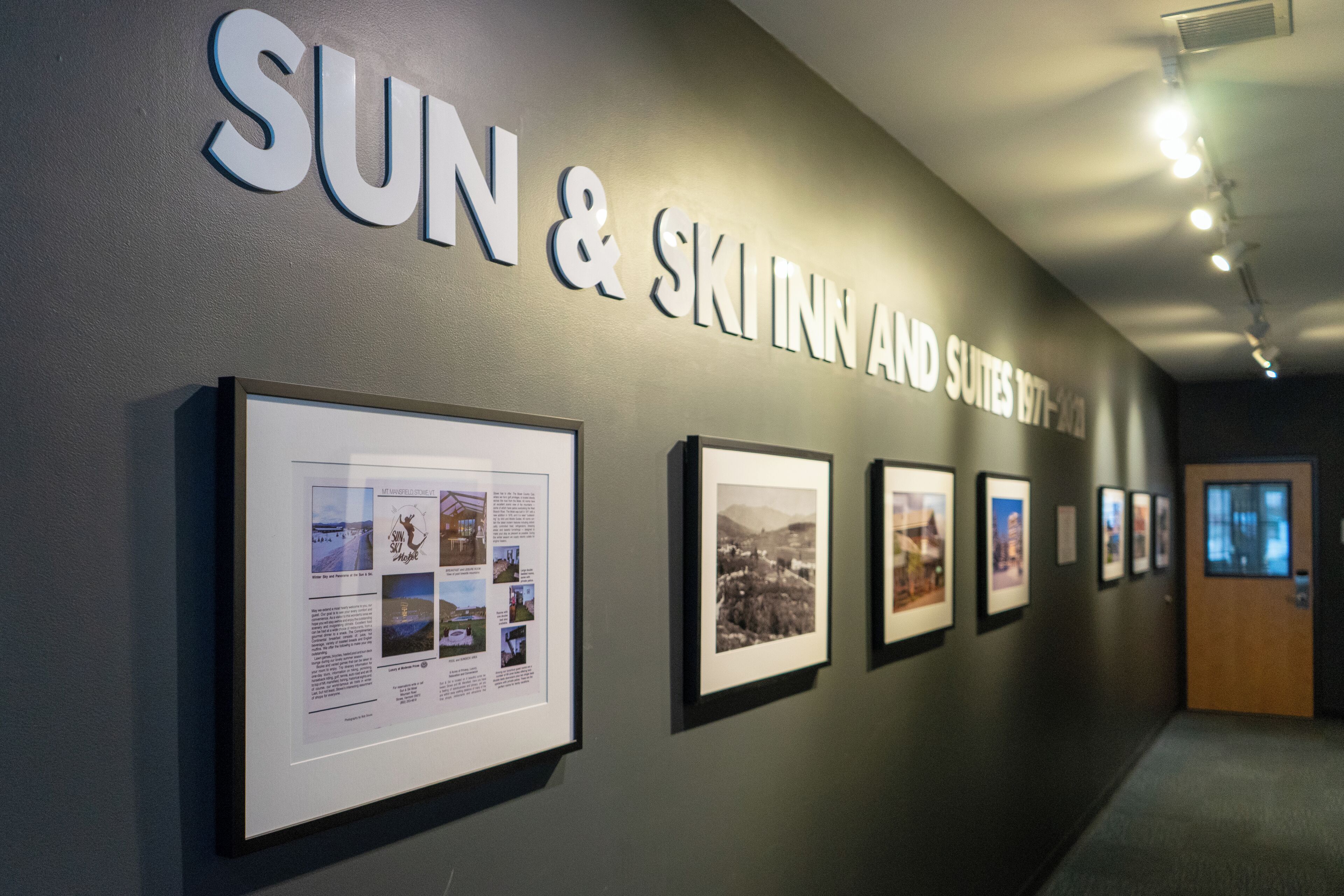 Un pasillo con un cartel que dice “SUN & SKI INN AND SUITES 1977-2023” y fotografías enmarcadas en la pared.