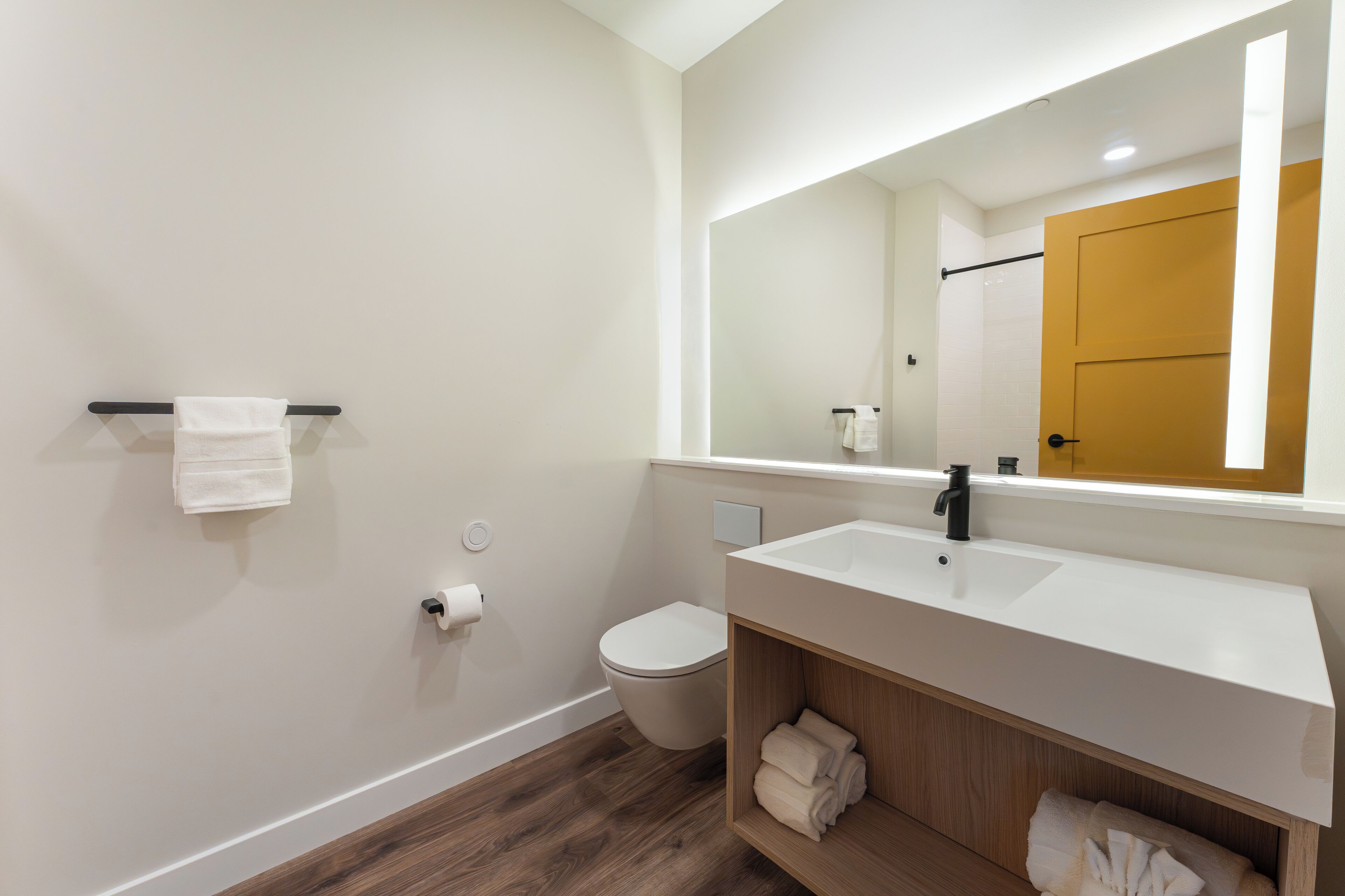 A modern bathroom with a white sink, wooden vanity, and a towel rack.