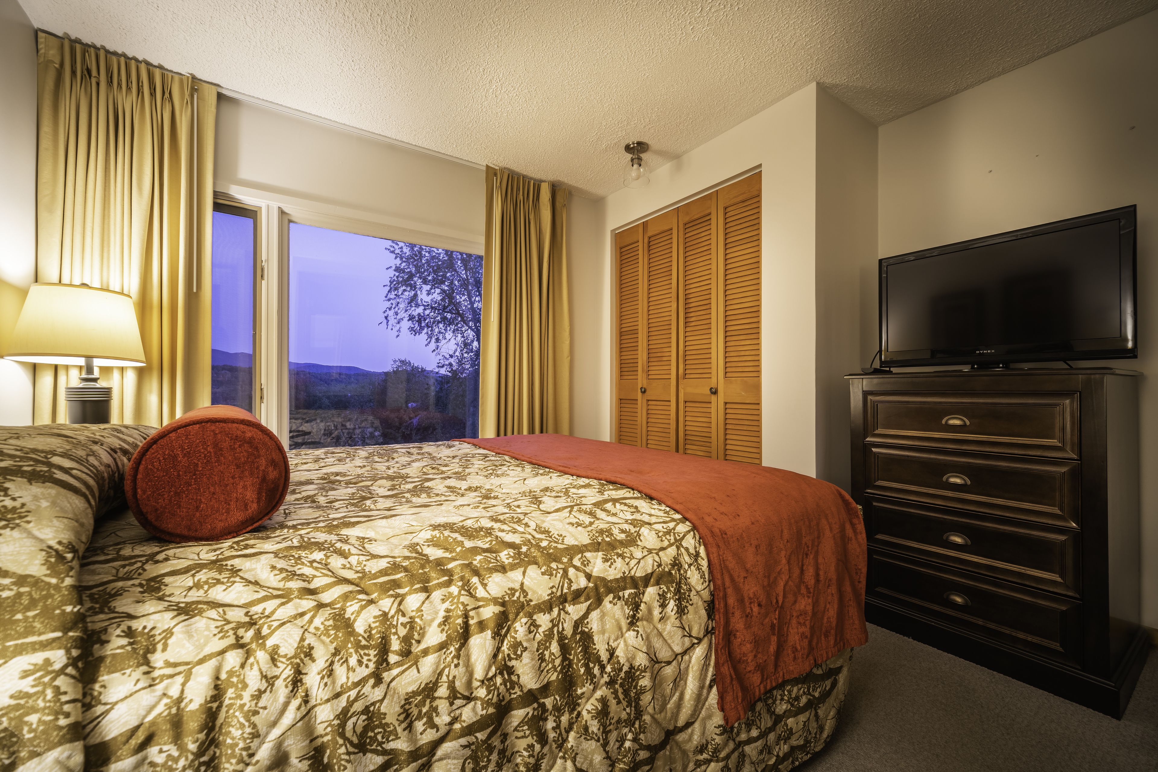 A hotel room with a bed, a dresser, a television, and a window with curtains.