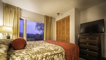 A hotel room with a bed, a dresser, a television, and a window with curtains.