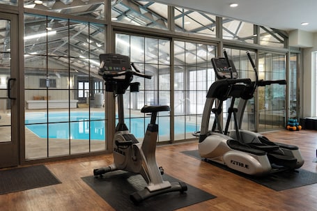 An indoor gym with two exercise bikes and a view of an indoor pool through large windows.
