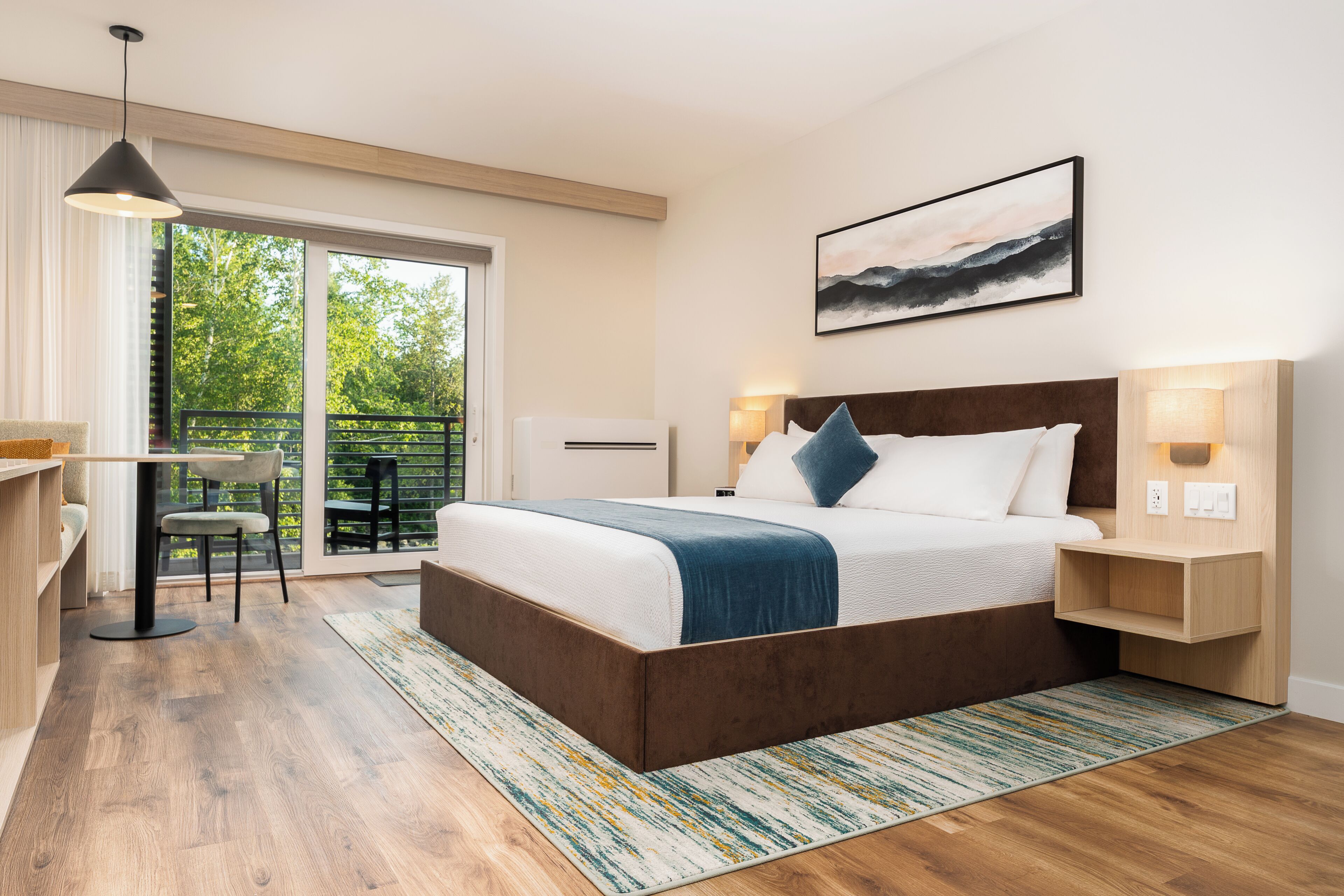 A modern bedroom with a large bed, bedside lamps, a desk, and a view of greenery through the window.